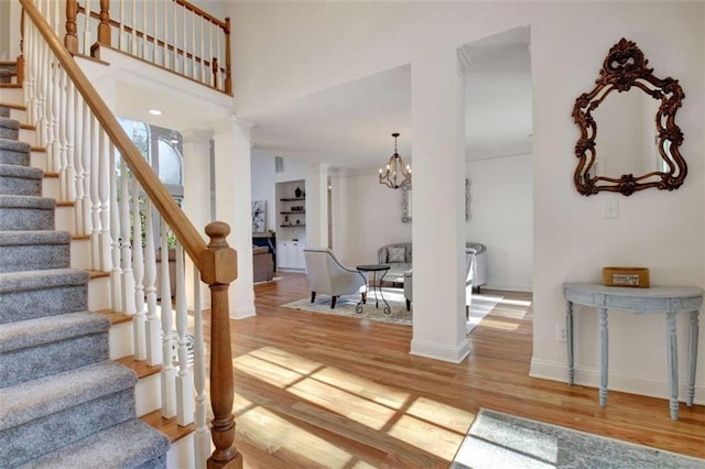 foyer featuring an inviting chandelier, wood-type flooring, and decorative columns