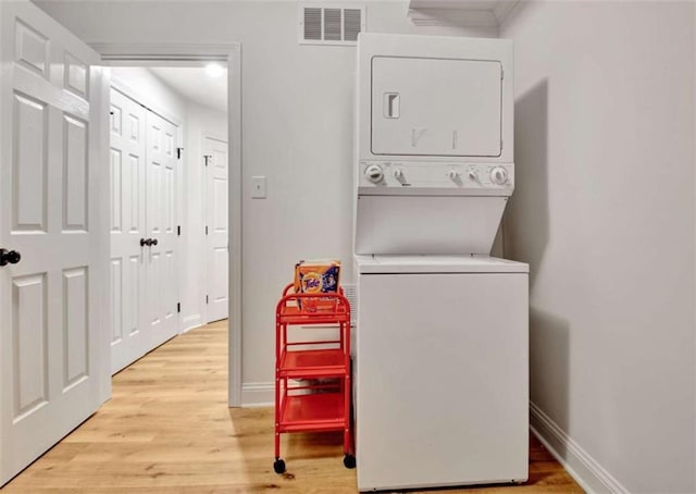 laundry room with light hardwood / wood-style floors and stacked washing maching and dryer