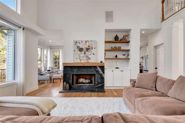 living room with built in shelves, light hardwood / wood-style floors, a premium fireplace, and a towering ceiling