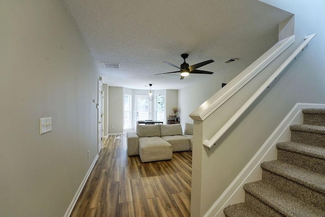 stairs featuring a ceiling fan, a textured ceiling, visible vents, wood finished floors, and baseboards