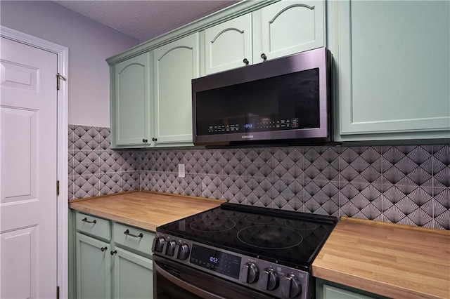 kitchen with butcher block countertops, appliances with stainless steel finishes, tasteful backsplash, and green cabinets