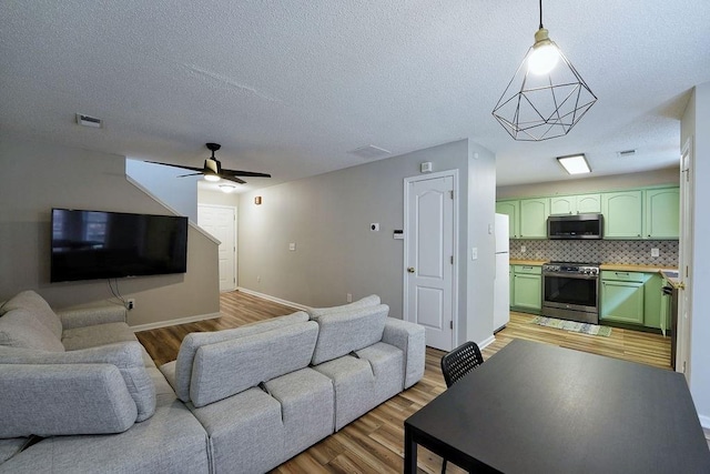 living area featuring visible vents, a ceiling fan, light wood finished floors, and baseboards