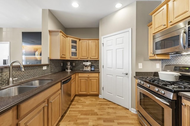 kitchen with dark stone countertops, light wood finished floors, a sink, appliances with stainless steel finishes, and backsplash