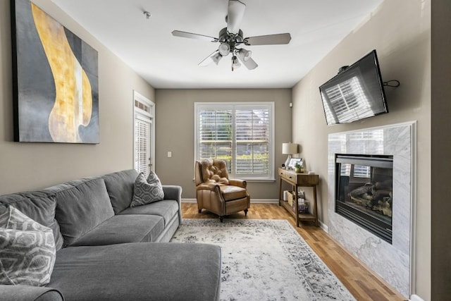 living room with baseboards, light wood-style floors, ceiling fan, and a fireplace