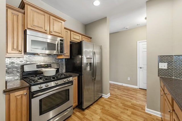 kitchen with dark stone countertops, baseboards, decorative backsplash, light wood-style floors, and appliances with stainless steel finishes