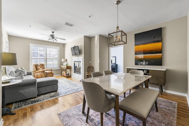 dining space with visible vents, baseboards, ceiling fan with notable chandelier, a fireplace, and wood finished floors