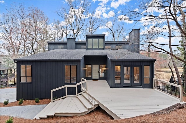 back of property featuring french doors, a deck, a chimney, and a shingled roof