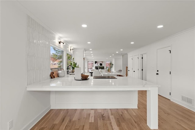 kitchen with visible vents, a peninsula, light wood-style floors, and ornamental molding