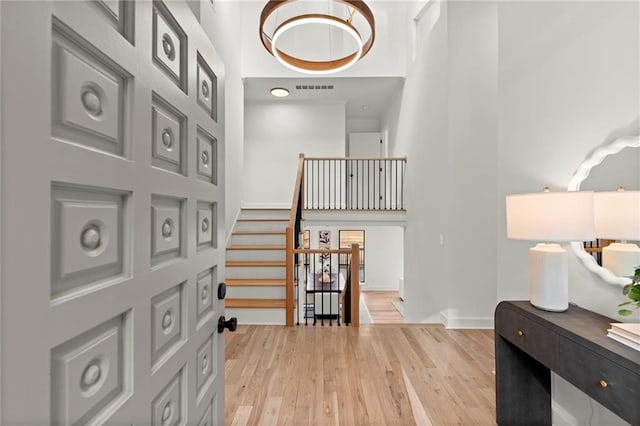 entryway with visible vents, baseboards, stairway, light wood-type flooring, and a towering ceiling