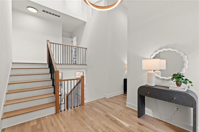 stairway featuring a high ceiling, wood finished floors, visible vents, and baseboards