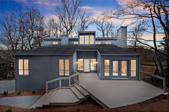 back of house at dusk with french doors, a chimney, and a wooden deck