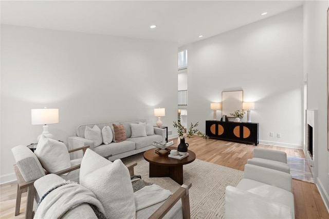 living room featuring recessed lighting, baseboards, light wood-type flooring, and a high ceiling