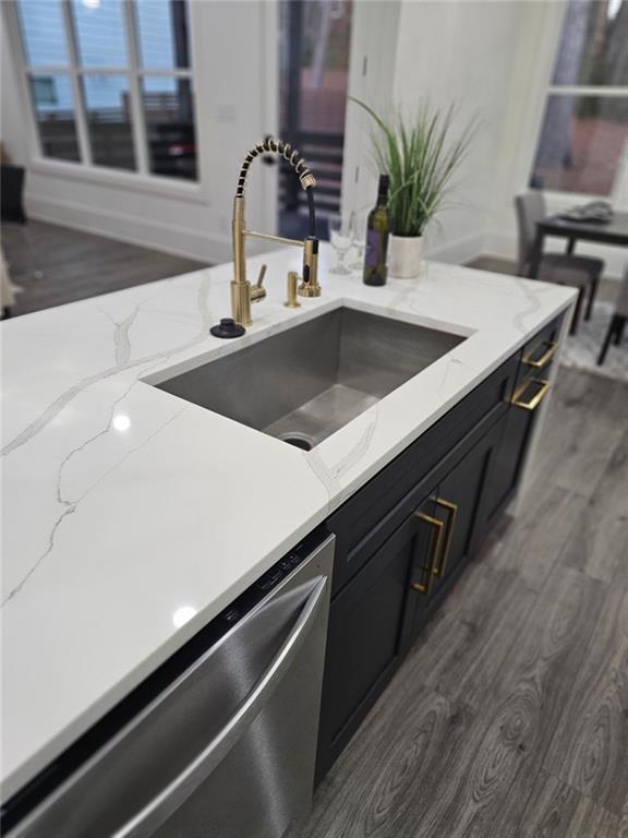 kitchen featuring dark hardwood / wood-style flooring, dishwasher, sink, and light stone countertops