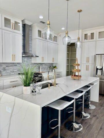 kitchen with pendant lighting, appliances with stainless steel finishes, a kitchen island with sink, white cabinetry, and wall chimney exhaust hood