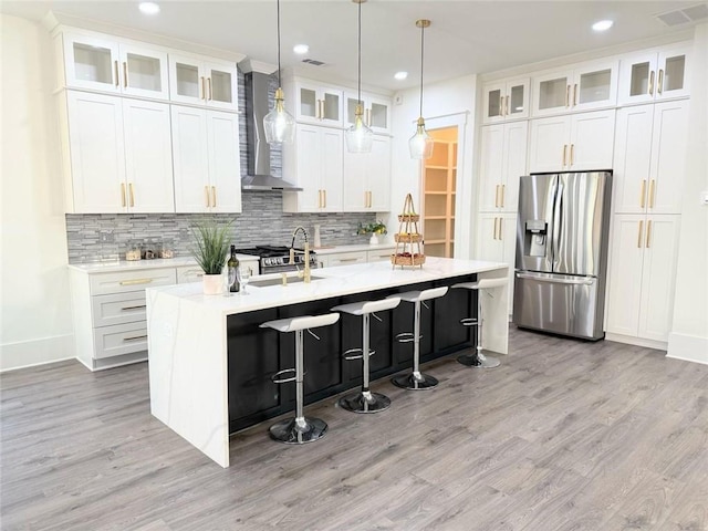 kitchen with wall chimney range hood, stainless steel appliances, white cabinets, and a center island with sink