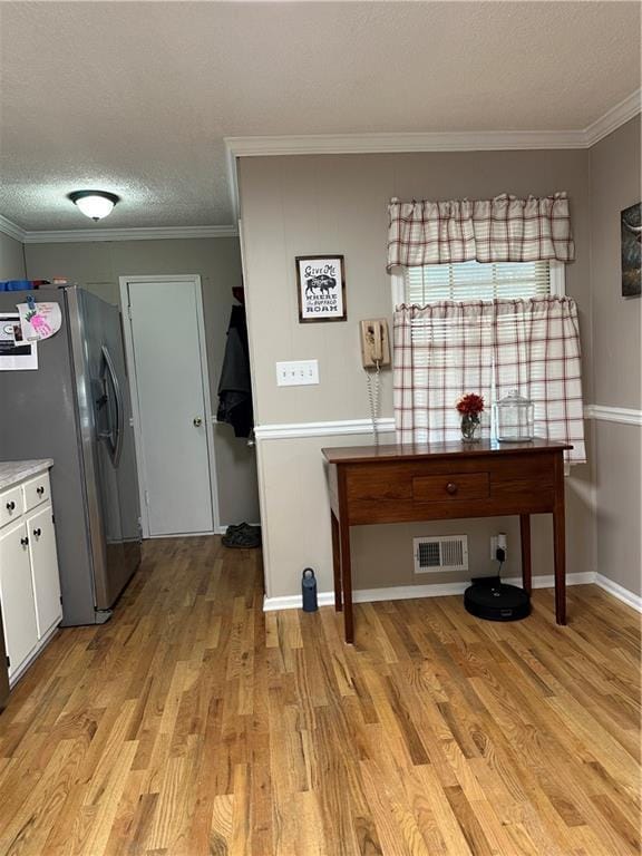 kitchen with stainless steel refrigerator with ice dispenser, light wood-type flooring, white cabinetry, a textured ceiling, and ornamental molding