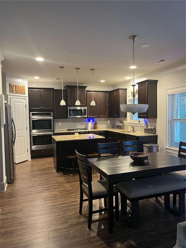 2208 Ginger Lake Dr NE, Conyers, GA 30013 - kitchen featuring appliances with stainless steel finishes, a kitchen island, ornamental molding, dark wood-style flooring, and dark brown cabinets