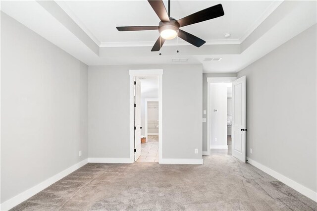 unfurnished bedroom featuring a tray ceiling, ensuite bath, ceiling fan, and light colored carpet