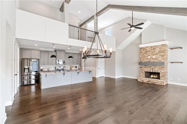 unfurnished living room with ceiling fan with notable chandelier, dark hardwood / wood-style flooring, high vaulted ceiling, and a brick fireplace