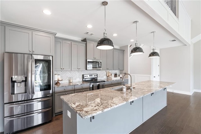 kitchen featuring sink, dark wood-type flooring, a kitchen bar, a center island with sink, and appliances with stainless steel finishes