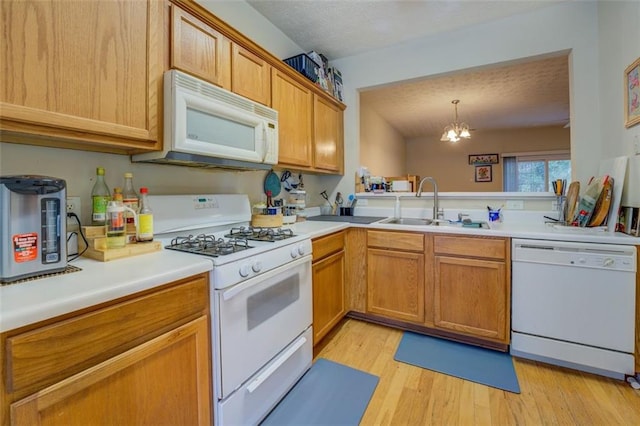 kitchen featuring white appliances, sink, decorative light fixtures, an inviting chandelier, and light hardwood / wood-style floors