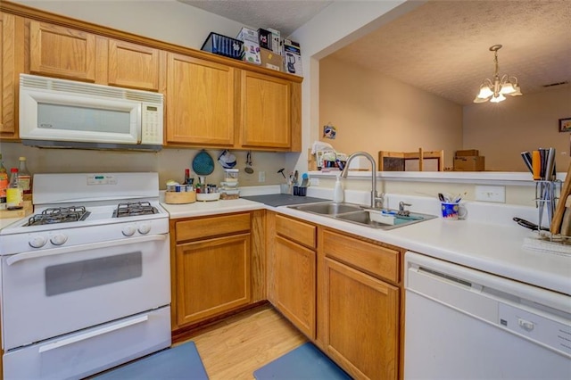 kitchen featuring light wood-type flooring, white appliances, sink, pendant lighting, and a notable chandelier