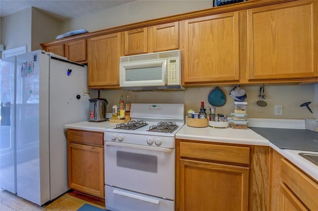 kitchen featuring light wood-type flooring, a textured ceiling, and white appliances