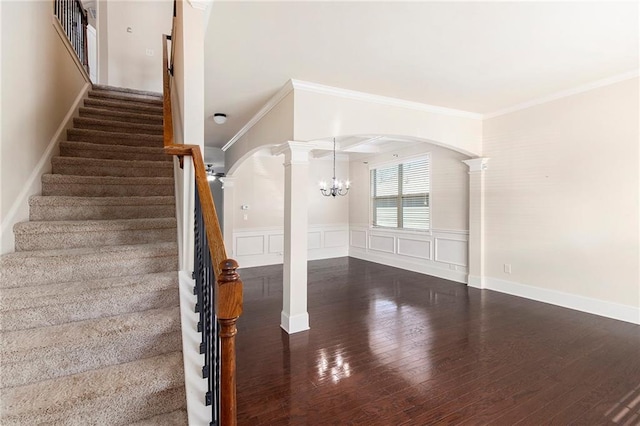 staircase featuring a notable chandelier, crown molding, wood-type flooring, and decorative columns