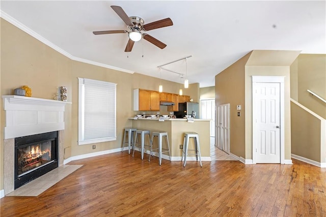 kitchen with a kitchen bar, kitchen peninsula, stainless steel fridge, ceiling fan, and a fireplace