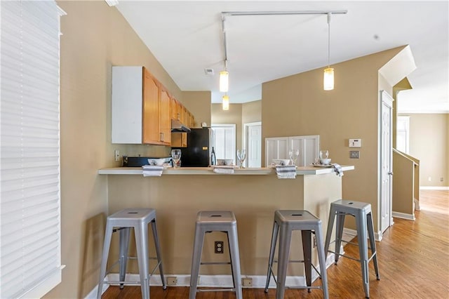 kitchen featuring light hardwood / wood-style floors, a breakfast bar area, light brown cabinets, black fridge, and hanging light fixtures