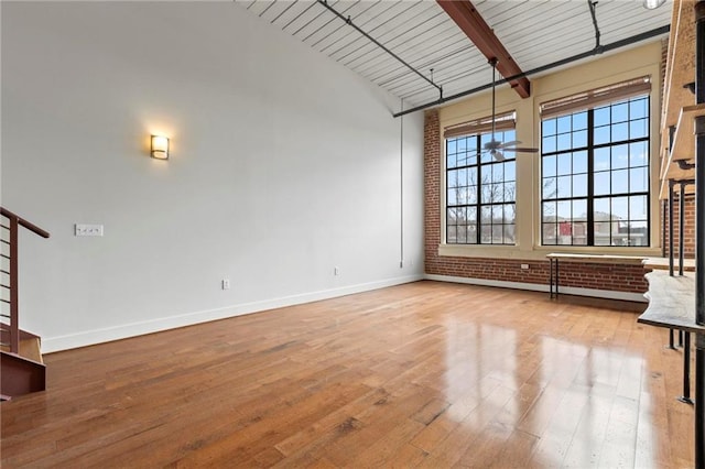 unfurnished living room featuring wood ceiling, brick wall, light hardwood / wood-style flooring, and vaulted ceiling with beams