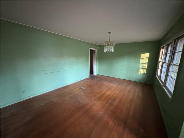 unfurnished room with wood finished floors and an inviting chandelier