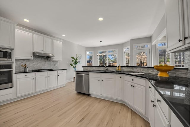 kitchen with light wood finished floors, stainless steel appliances, white cabinets, a peninsula, and under cabinet range hood