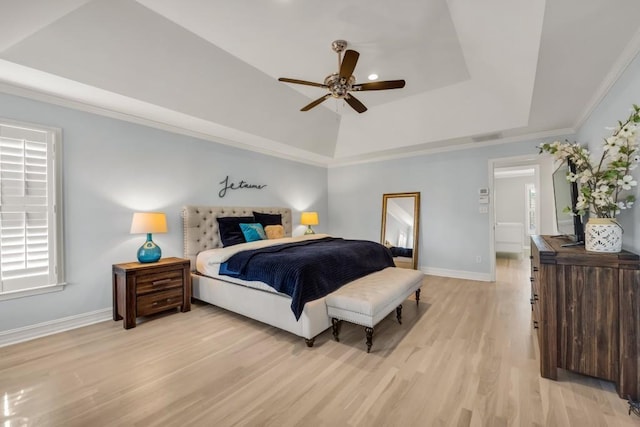 bedroom featuring a ceiling fan, baseboards, light wood-style floors, ornamental molding, and a tray ceiling