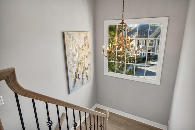 stairs with a chandelier, a wealth of natural light, baseboards, and wood finished floors