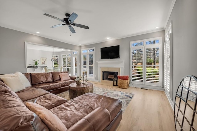 living room with ornamental molding, wood finished floors, ceiling fan with notable chandelier, a fireplace, and recessed lighting