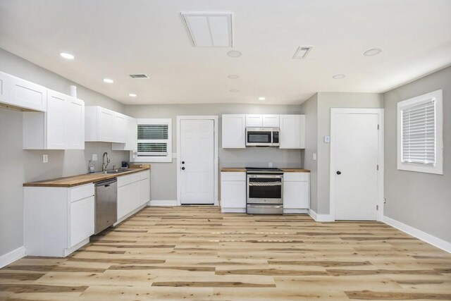 kitchen with white cabinets, light hardwood / wood-style flooring, butcher block counters, sink, and stainless steel appliances