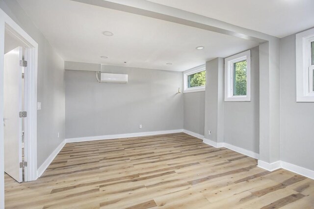 basement with a wall mounted AC and light wood-type flooring