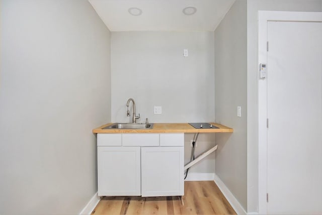 bar with butcher block counters, sink, light hardwood / wood-style floors, and white cabinets