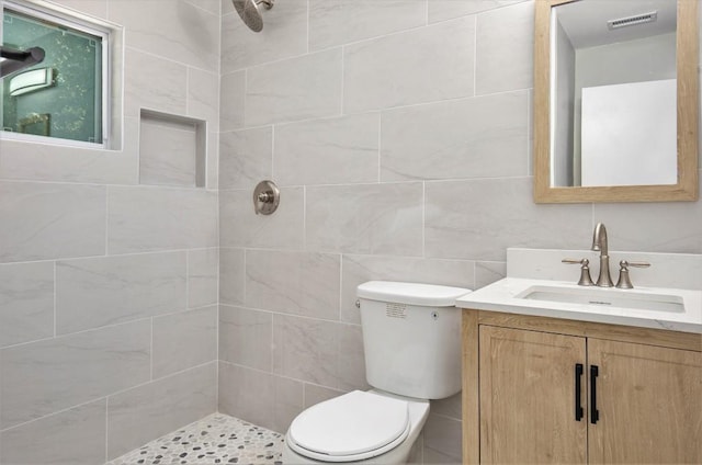 bathroom with tile walls, vanity, a tile shower, and toilet