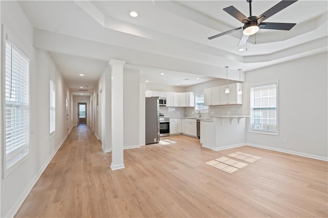 kitchen with pendant lighting, light wood-type flooring, appliances with stainless steel finishes, tasteful backsplash, and white cabinetry