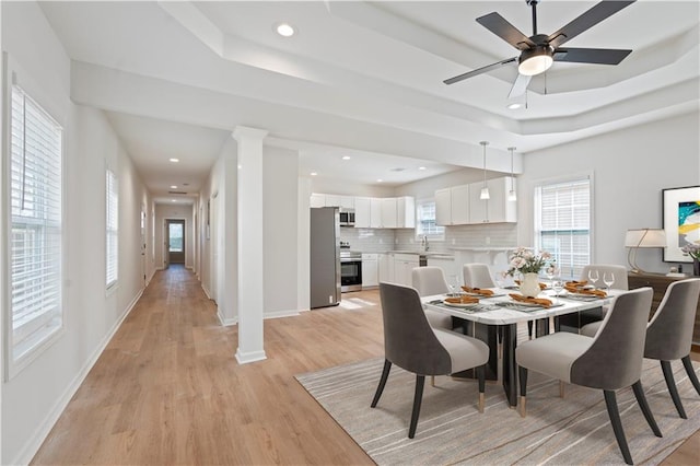 dining space with ceiling fan, light hardwood / wood-style floors, a raised ceiling, and ornate columns