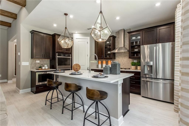 kitchen featuring dark brown cabinets, appliances with stainless steel finishes, light countertops, and wall chimney range hood