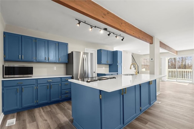 kitchen with blue cabinetry, dark wood finished floors, beamed ceiling, stainless steel appliances, and a sink