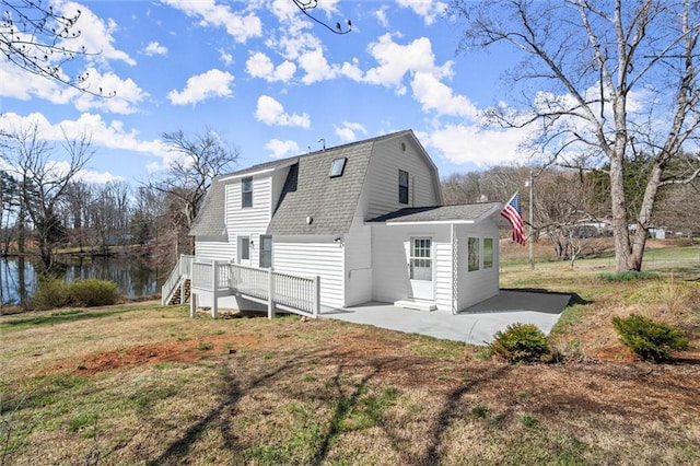 rear view of property with roof with shingles, a gambrel roof, a water view, a patio area, and a lawn