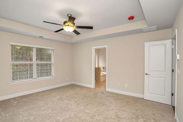 unfurnished bedroom featuring a tray ceiling, connected bathroom, light carpet, and ceiling fan