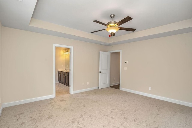 unfurnished bedroom featuring a raised ceiling, ensuite bathroom, ceiling fan, and light colored carpet