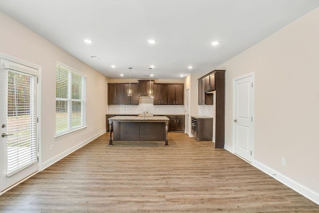 kitchen featuring a center island with sink, tasteful backsplash, decorative light fixtures, light hardwood / wood-style floors, and a breakfast bar area