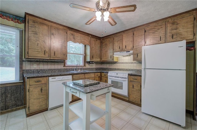 kitchen with light floors, dark countertops, a sink, white appliances, and under cabinet range hood