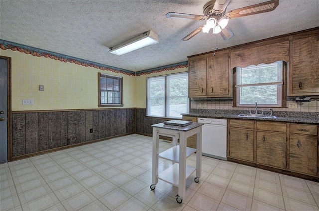 kitchen with light floors, wallpapered walls, dishwasher, and a wainscoted wall